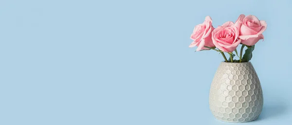 Beautiful pink roses in vase on light blue background with space for text