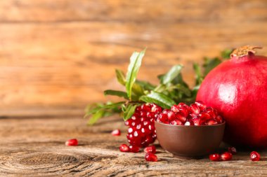 Bowl of pomegranate seeds on wooden background clipart