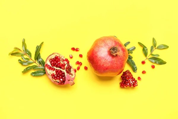 Composition with fresh pomegranates and plant branches on yellow background