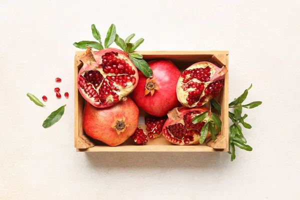 Wooden box with fresh pomegranates and plant branches on light background