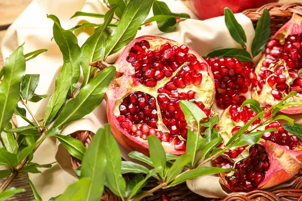 Wicker basket with fresh pomegranates and plant branches, closeup