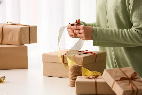 Woman cutting ribbon for Christmas gift box at table, closeup