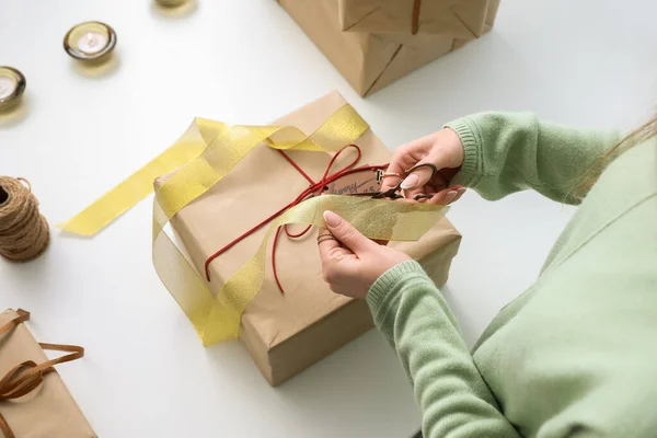 Woman cutting ribbon for Christmas gift box at white table, closeup
