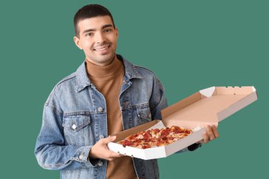 Yeşil arka planda taze pizza kutulu yakışıklı genç adam.