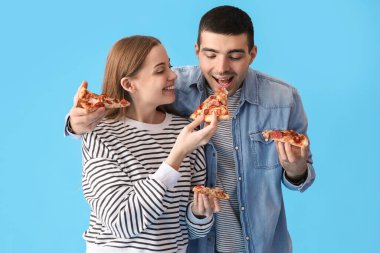 Mutlu genç çift mavi arka planda taze pizza yiyor.