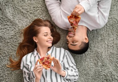 Halıda uzanmış pizza dilimleriyle mutlu genç bir çift.
