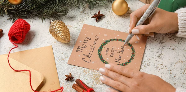 テーブルでメリークリスマスとハッピーニューイヤーのためのペンとグリーティングカードを持つ女性 — ストック写真