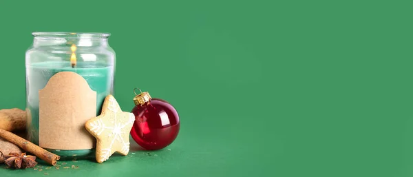 Stock image Jar with burning candle, cookies, cinnamon and Christmas ball on green background with space for text