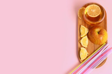 Tahta tahta tahta tahta, bir bardak taze elma suyu, limon dilimleri ve pembe arka planda pipetler.