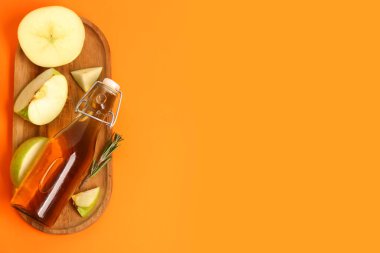 Olgun elmalı ahşap tahta ve renkli arkaplanlı bir şişe meyve suyu.