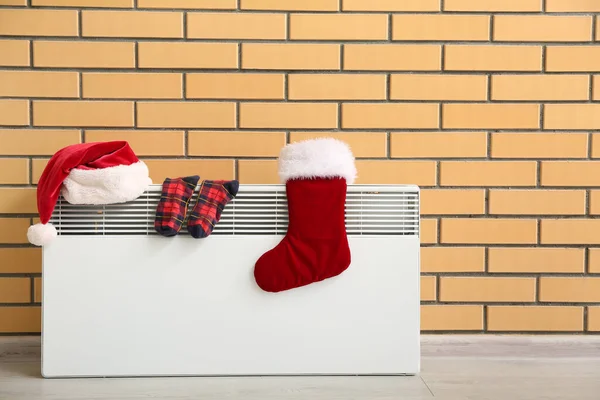 stock image Santa hat with warm socks drying on electric radiator near brick wall