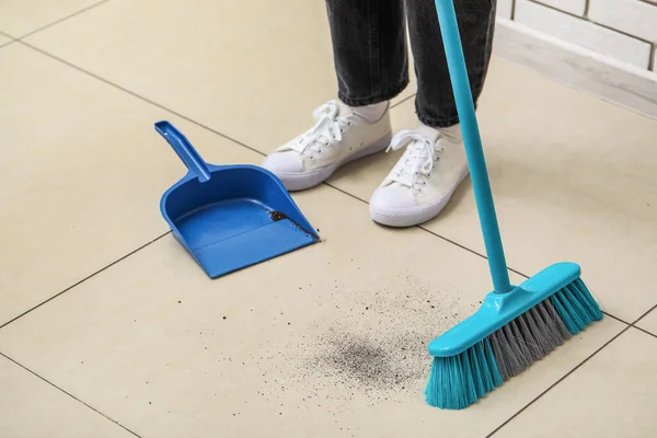 Woman sweeping light tile floor with broom and dustpan
