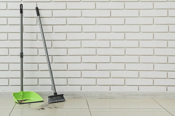 Dustpan with rubbish and cleaning broom near brick wall