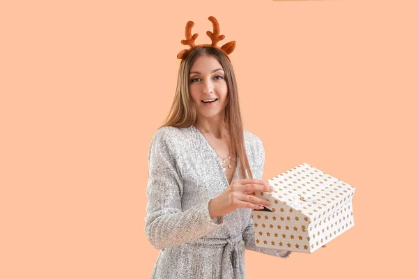 头戴驯鹿角的年轻女子在米色背景下打开圣诞礼物 — 图库照片