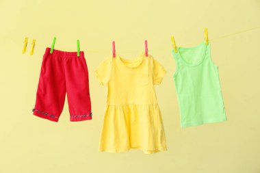 Sarı arka planda ipte asılı farklı bebek kıyafetleri.