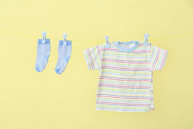Bebek kıyafetleri sarı arka planda çamaşır ipine asılı.