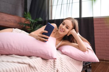 Evdeki yatakta cep telefonu kullanan güzel bir genç kadın.