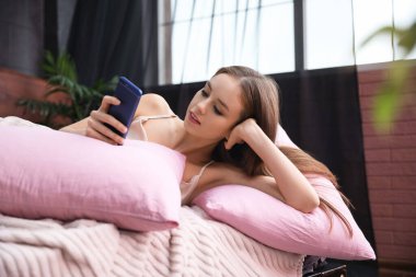 Evdeki yatakta cep telefonu kullanan güzel bir genç kadın.
