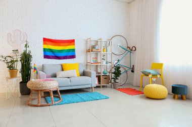 Rahat kanepesi, raf ünitesi, bisikleti ve gökkuşağı bayrakları olan modern oturma odasının içinde.