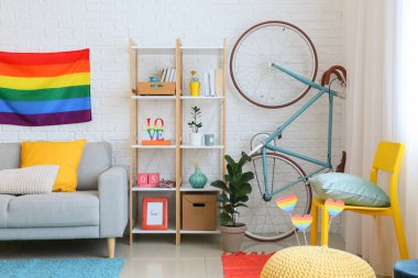 Raflar, kanepe, bisiklet ve gökkuşağı bayrakları beyaz tuğla duvarın yanında.