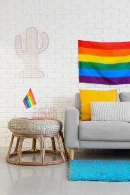 Rahat kanepe, puf ve gökkuşağı bayrakları beyaz tuğla duvarın yanında.