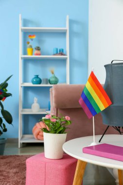 Güzel bir çiçek, raflama ünitesi ve masa üzerinde gökkuşağı bayrağı olan modern bir lamba.