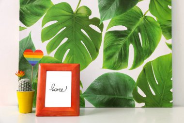 Güzel kaktüs, gökkuşağı bayrağı, resim ve fotoğraf çerçevesi beyaz duvarın yanındaki masada.