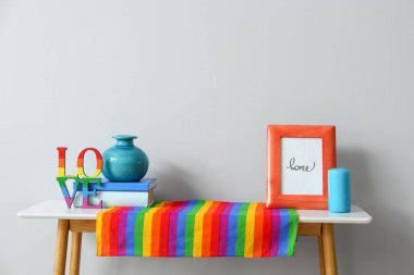 Gökkuşağı bayrağı, fotoğraf çerçevesi, mum ve vazo ışık duvarının yanındaki masada.