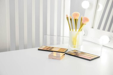 Makyaj fırçası ve göz farı olan bir tutucu odadaki makyaj sanatçısının masasında.
