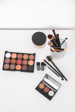 Makyaj sanatçılarının beyaz masasında fırça ve dekoratif kozmetik ürünleri olan tutucu.