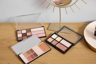 Dekoratif kozmetik ürünleri ve ayna ışık duvarının yanındaki ahşap masada, yakın plan.