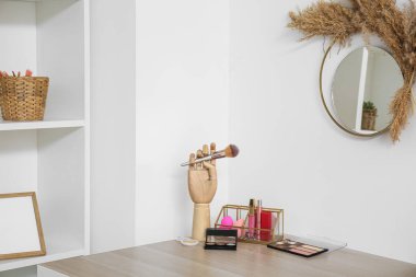 Makyaj fırçası ve dekoratif makyaj malzemesi olan tutucular ışık duvarının yanındaki masada.