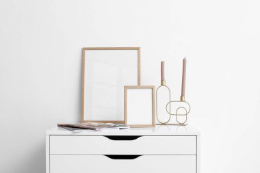 Boş çerçeveli göğüs çekmeceleri, mumlar, dergiler ve gözlüklerle aydınlık duvarın yanında.