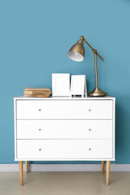 Boş çerçeveler, lamba ve mavi duvarın yanındaki çekmeceler üzerine kitaplar.