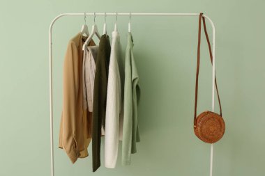 Yeşil duvarın yanında şık kıyafetler ve çantalar var.