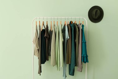 Yeşil duvarın yanında giysiler ve şapkayla dizilin.