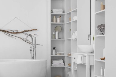 Modern küvet, lavabo ve raf üniteleri ve beyaz duvarın yanında banyo aksesuarları.