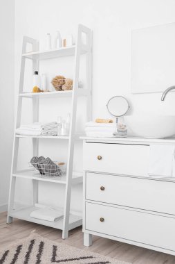 Modern lavabosu olan çekmeceler ve beyaz duvarın yanında banyo aksesuarları olan raf.