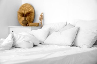 Beyaz duvarın yanında yumuşak çarşafları olan rahat bir yatak.