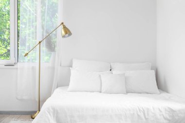 Yatak odasındaki beyaz duvarın yanında yumuşak çarşafları olan rahat bir yatak.