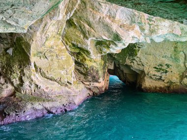 Mavi deniz suyu olan bir göl, uçurumdaki mağaranın manzarası
