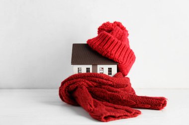 Beyaz ahşap arka planda şapkası ve eşarbı olan ev modeli. Isıtma kavramı