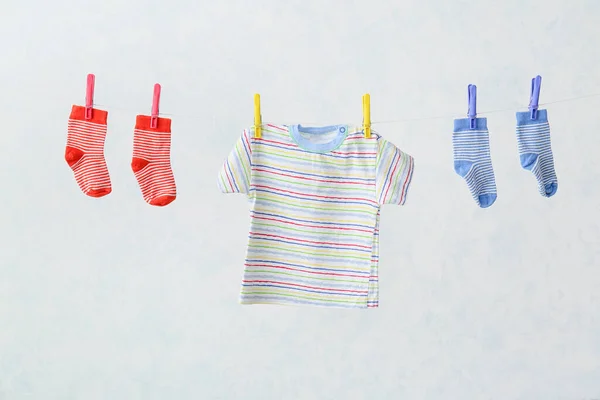 Baby clothes hanging on rope against light background