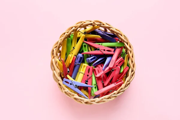 Basket with plastic clothespins on pink background
