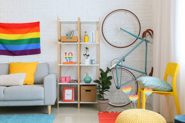 Raflar, kanepe, bisiklet ve gökkuşağı bayrakları beyaz tuğla duvarın yanında.