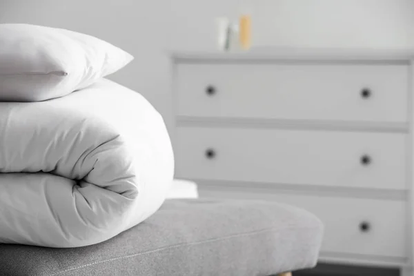 Folded white blanket and pillow on bench in bedroom, closeup