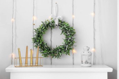 Şömine rafında mumları olan ve oturma odasında Noel çelengi asan bir fener.