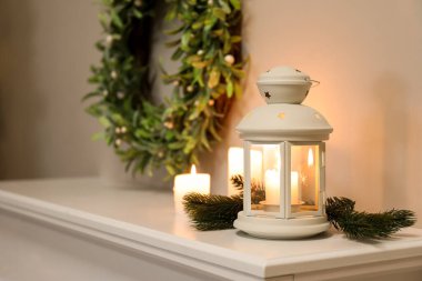 Oturma odasındaki şömine rafında mum ve köknar dalları olan Noel feneri, yakın plan.