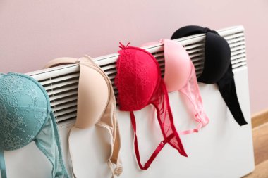 Pembe duvarın yanında elektrikli radyatörde kurutulan kadın sutyenler, yakın plan.