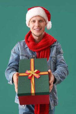 Yeşil arka planda Noel hediyesi olan Noel Baba şapkalı yakışıklı adam.